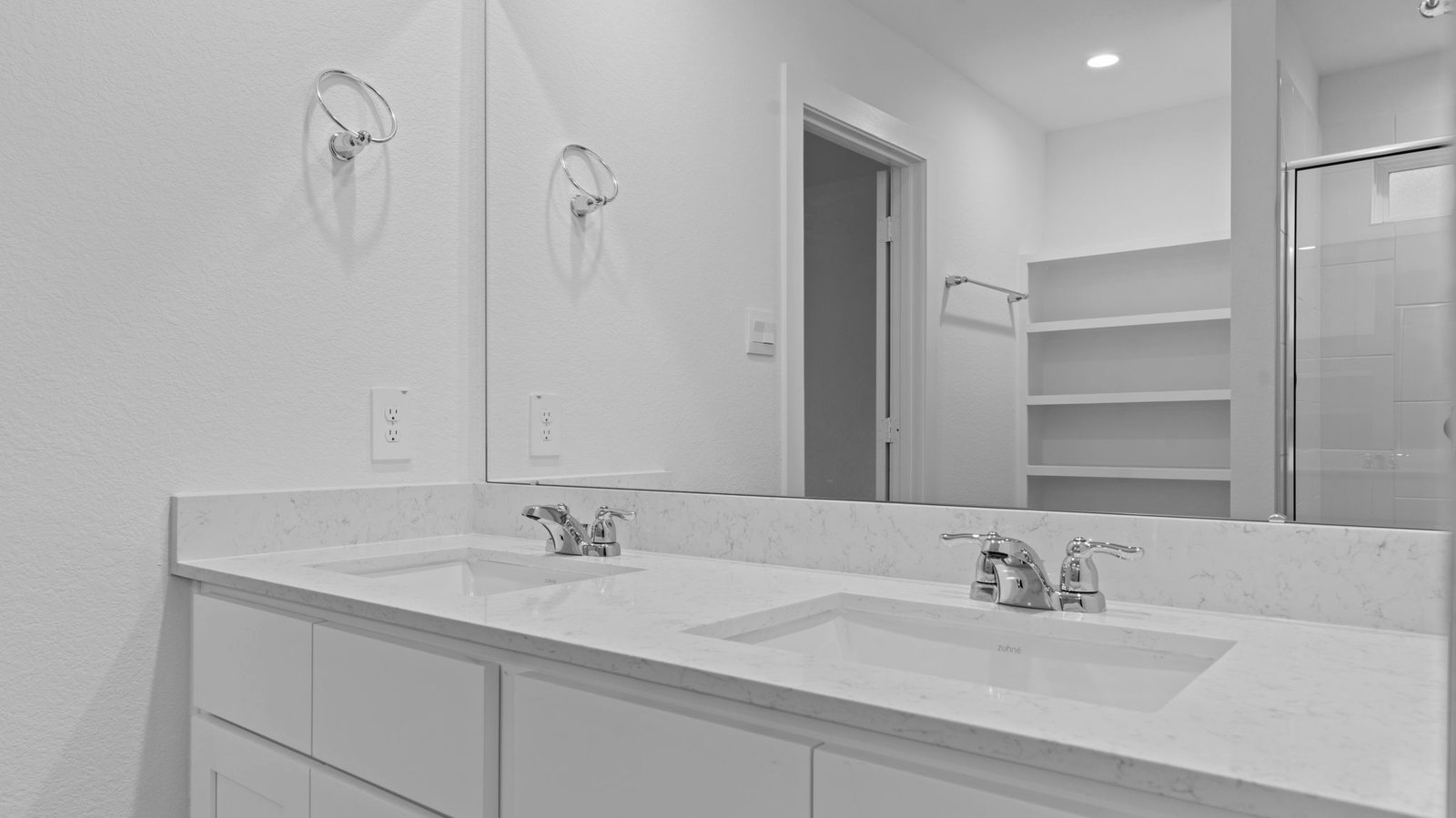 Modern primary bathroom with double vanities, quartz countertops, and a glass-enclosed shower with a walk-in closet.