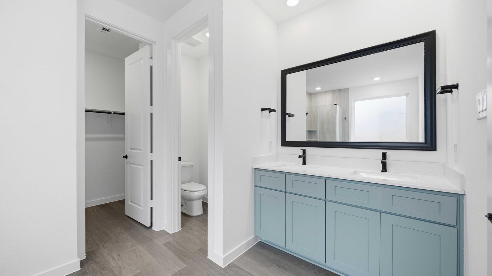 Modern primary bathroom with double vanities, quartz countertops, and a glass-enclosed shower with a walk-in closet.