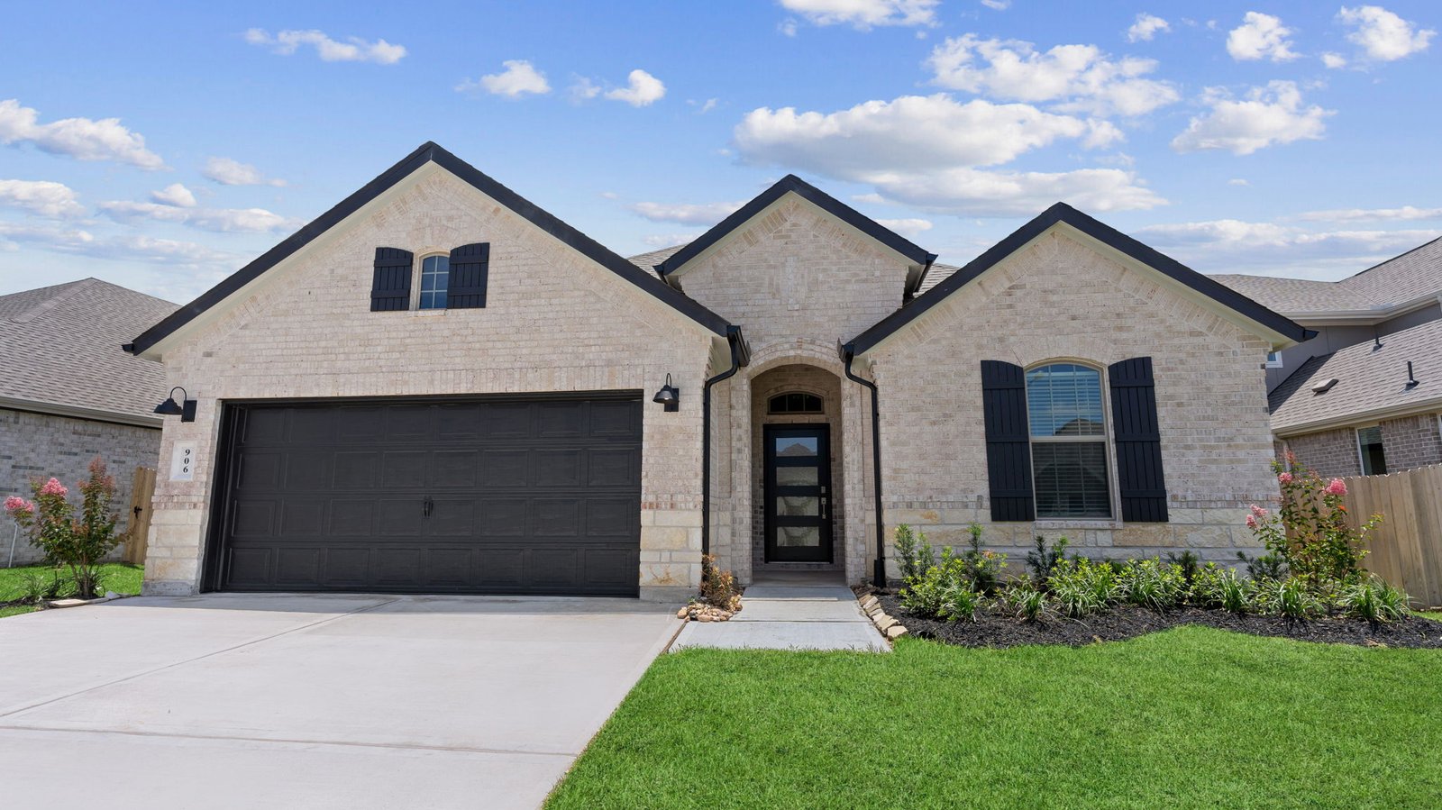 Single story home with a brick and stone exterior, three gables, two windows with shutters, split glass front door with a transom and a two-car garage.