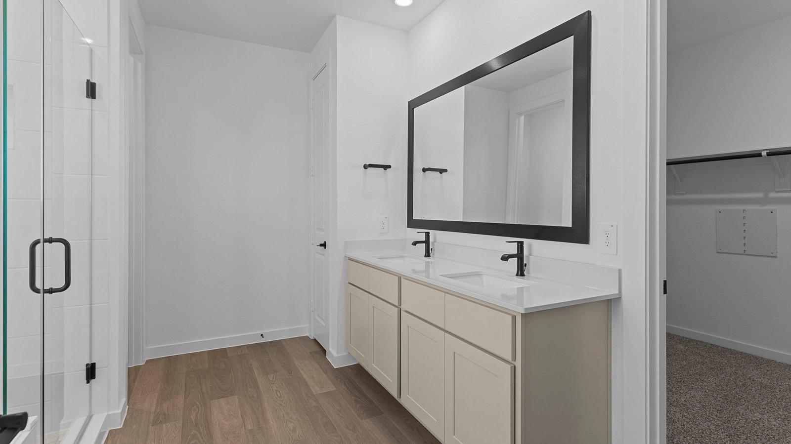 Modern primary bathroom with double vanities, quartz countertops, and a glass-enclosed shower with a walk-in closet.
