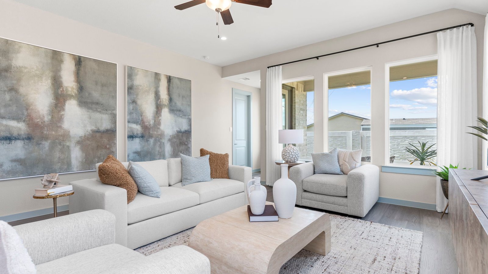 A cozy living room featuring large windows for natural lighting, wood flooring and a view to the kitchen and dining area.