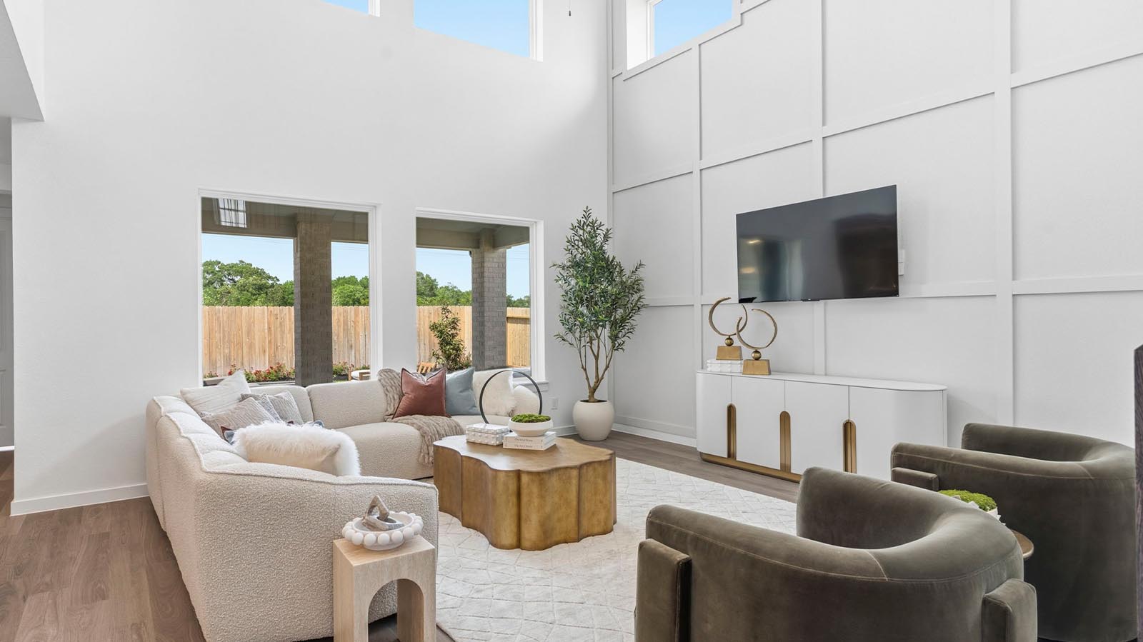 A luxurious living room featuring tall ceilings, large windows for natural lighting wood flooring and a view to the backyard.