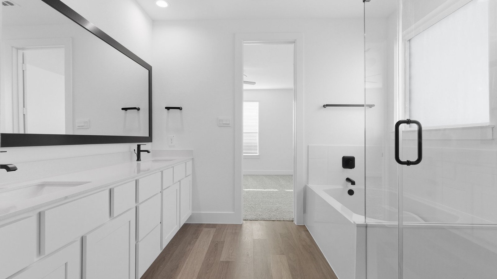 Modern primary bathroom with double vanities, quartz countertops, and a glass-enclosed shower with a walk-in closet.
