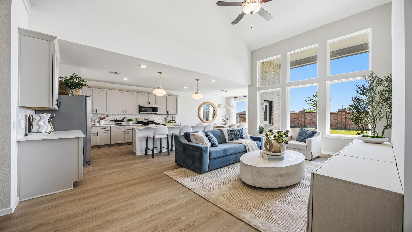 A luxurious living room featuring tall ceilings, large windows for natural lighting wood flooring and a view to the backyard.