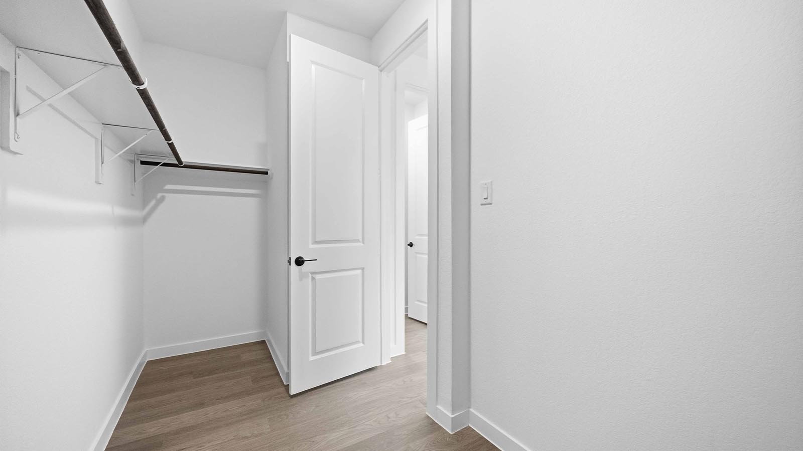 A spacious walk-in closet off the primary bathroom with multiple hanging rods, and shelves for maximum storage capabilities.