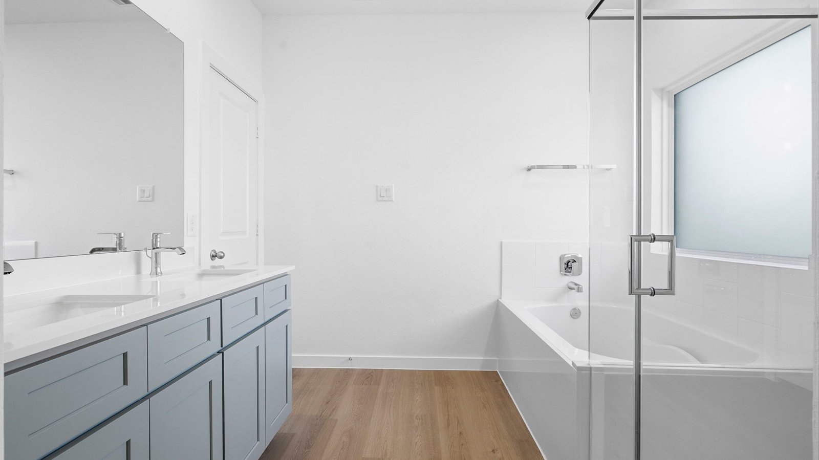 Modern primary bathroom with double vanities, quartz countertops, and a glass-enclosed shower with a walk-in closet