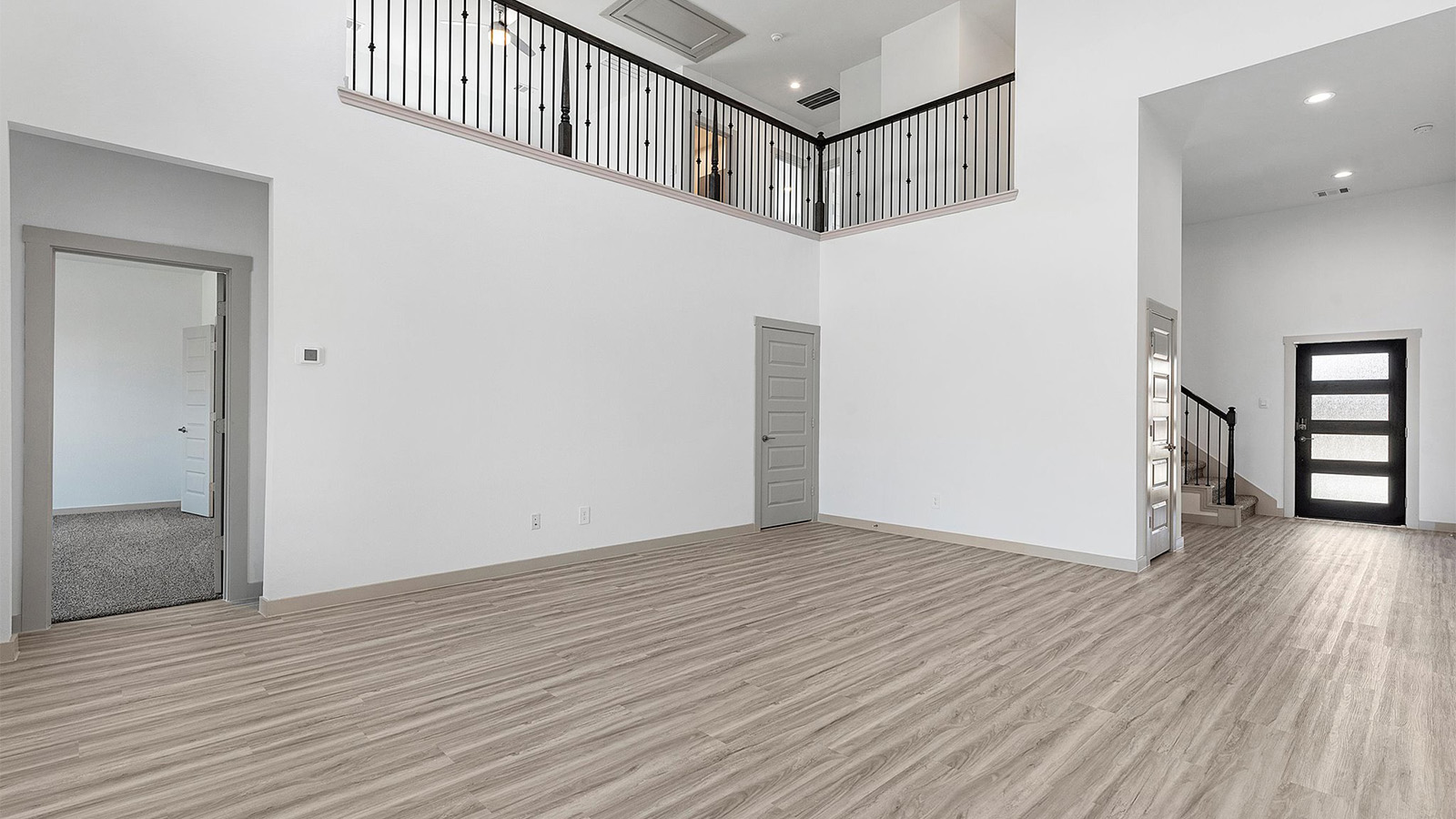A luxurious living room featuring tall ceilings, large windows for natural lighting wood flooring and a view to the backyard.