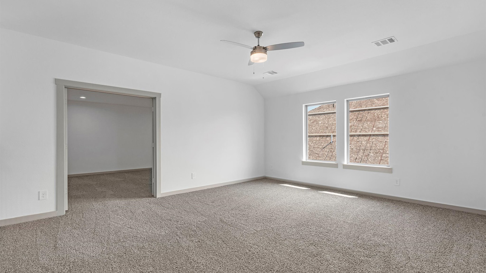 Primary bedroom with ceiling fan, plush carpeting, and a large walk-in closet.