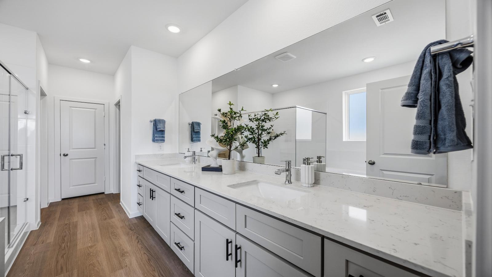 Modern primary bathroom with double vanities, quartz countertops, and a glass-enclosed shower with a walk-in closet.