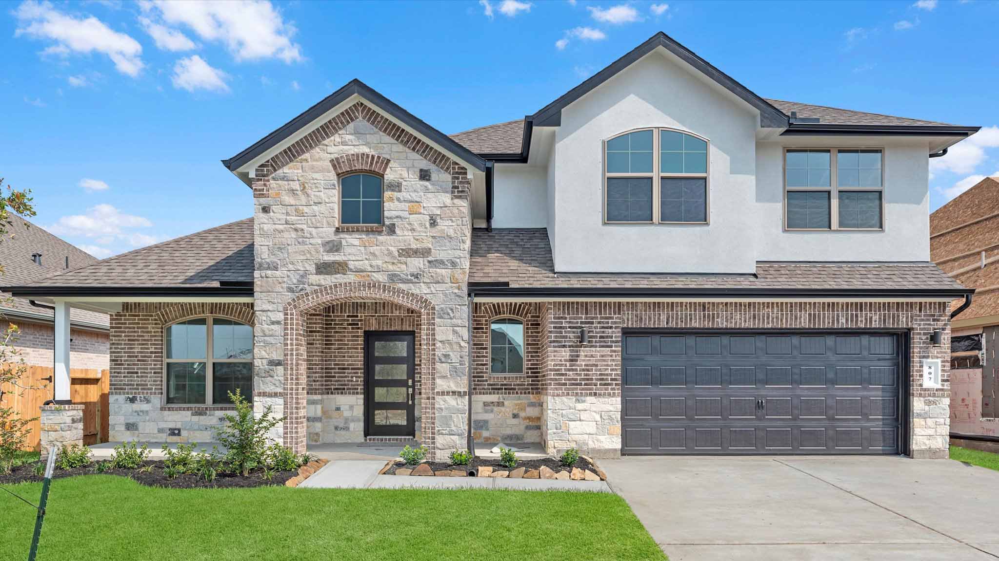 A two-story home with brick and stone exterior with a two-car garage and a well maintained front lawn in Texas City