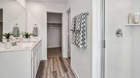 en-suite primary bathroom with walk-in shower with a glass enclosure and tile surround, and a double vanity with large mirror located above