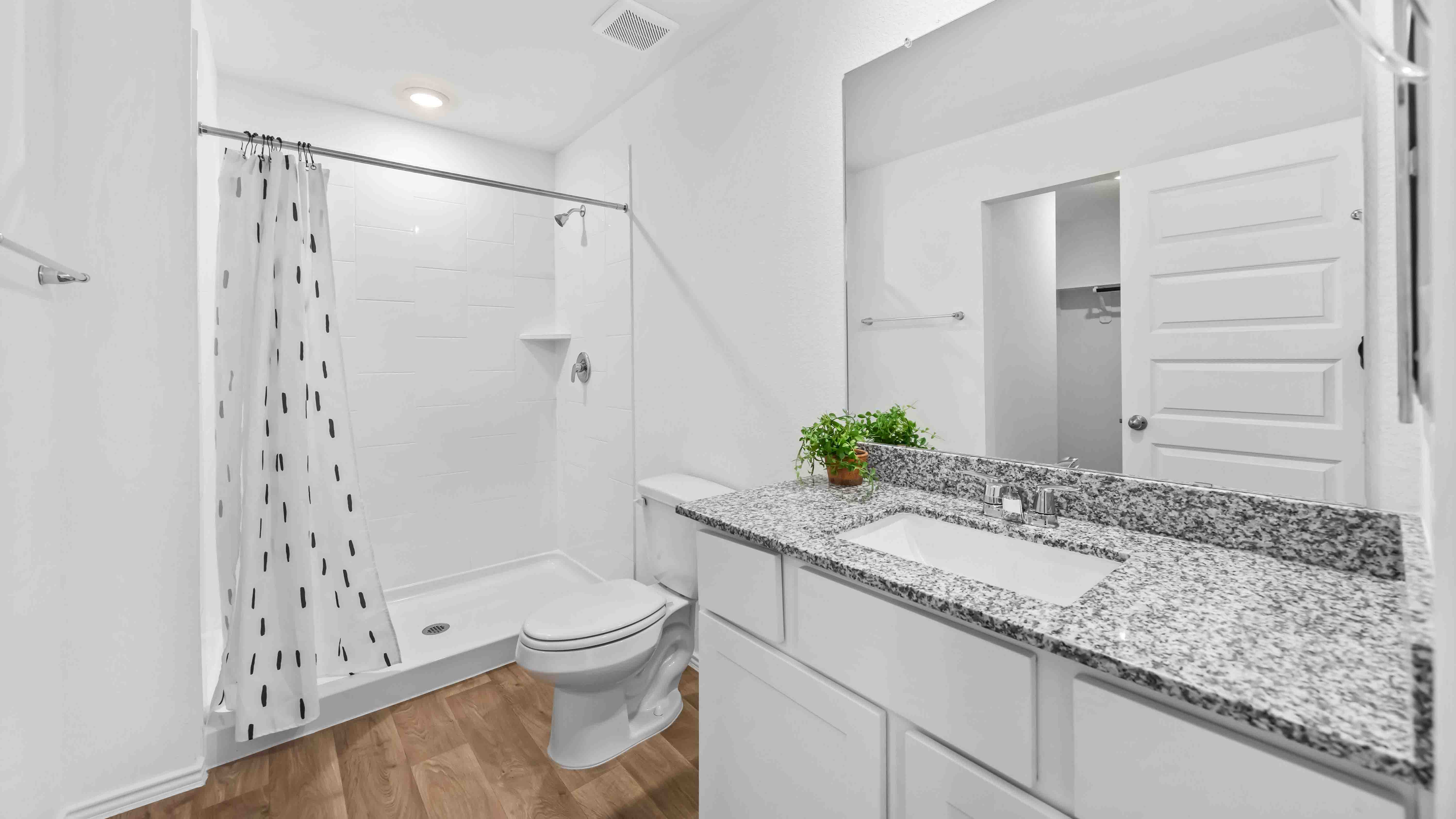 Modern primary bathroom with single vanity, granite countertops, and a standing shower with a walk-in closet.