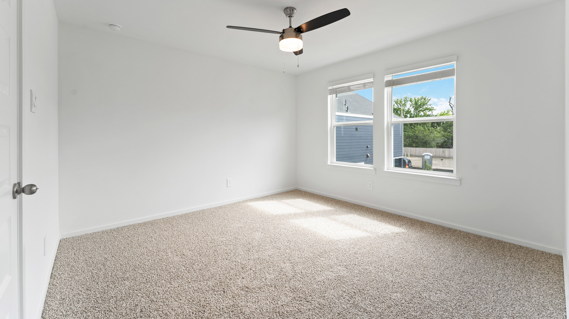 a spacious primary bedroom has two large windows and a ceiling fan installed