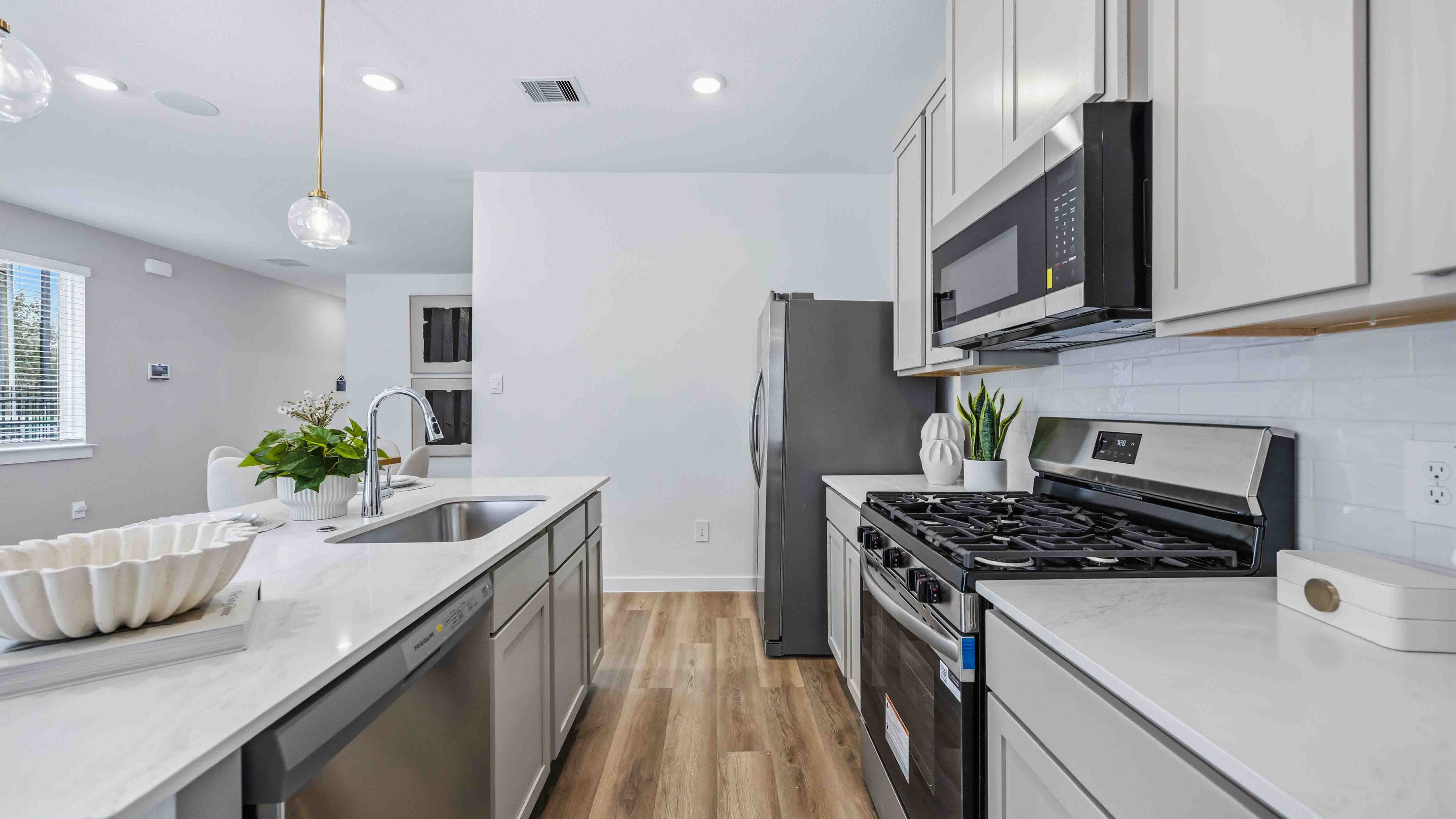beautiful new kitchen with quartz counters, light grey cabinets, and herringbone backsplash