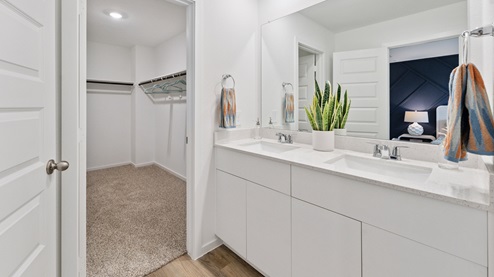 an en-suite primary bathroom has a large mirror over a double vanity and a walk-in shower