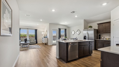 Kitchen island with brown cabinets and stainless steel appliances with views into the living area