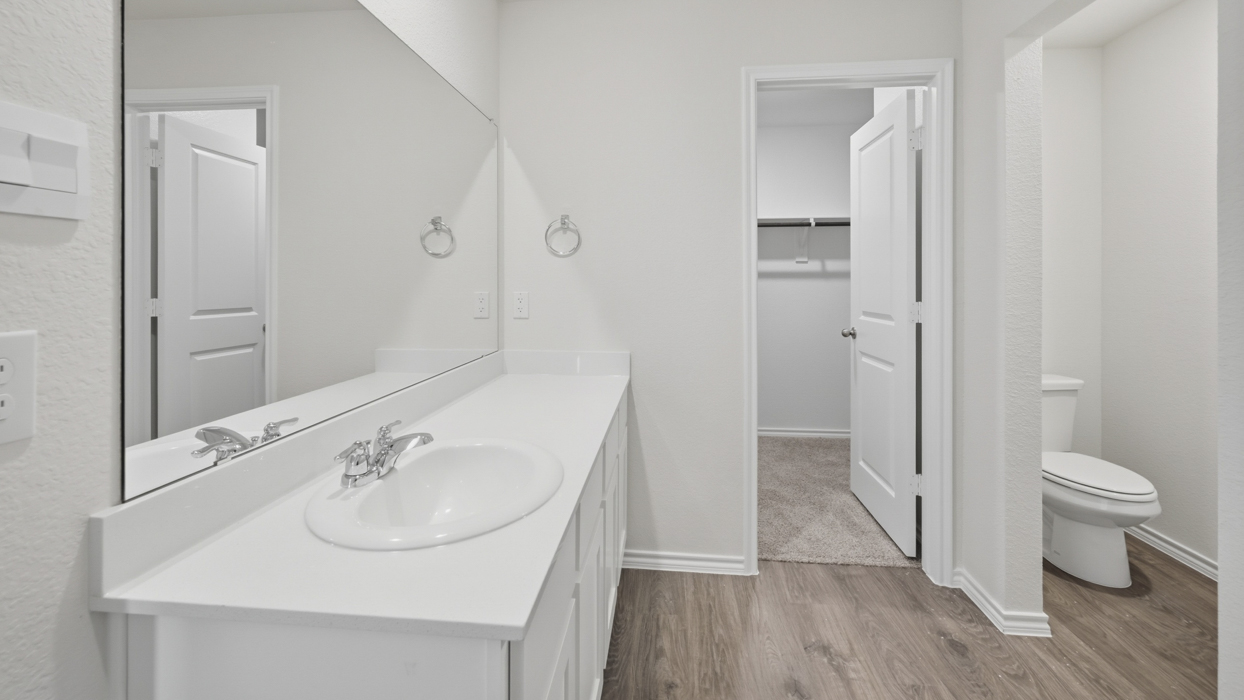 primary bathroom with white cabinets white countertops and walk in closet
