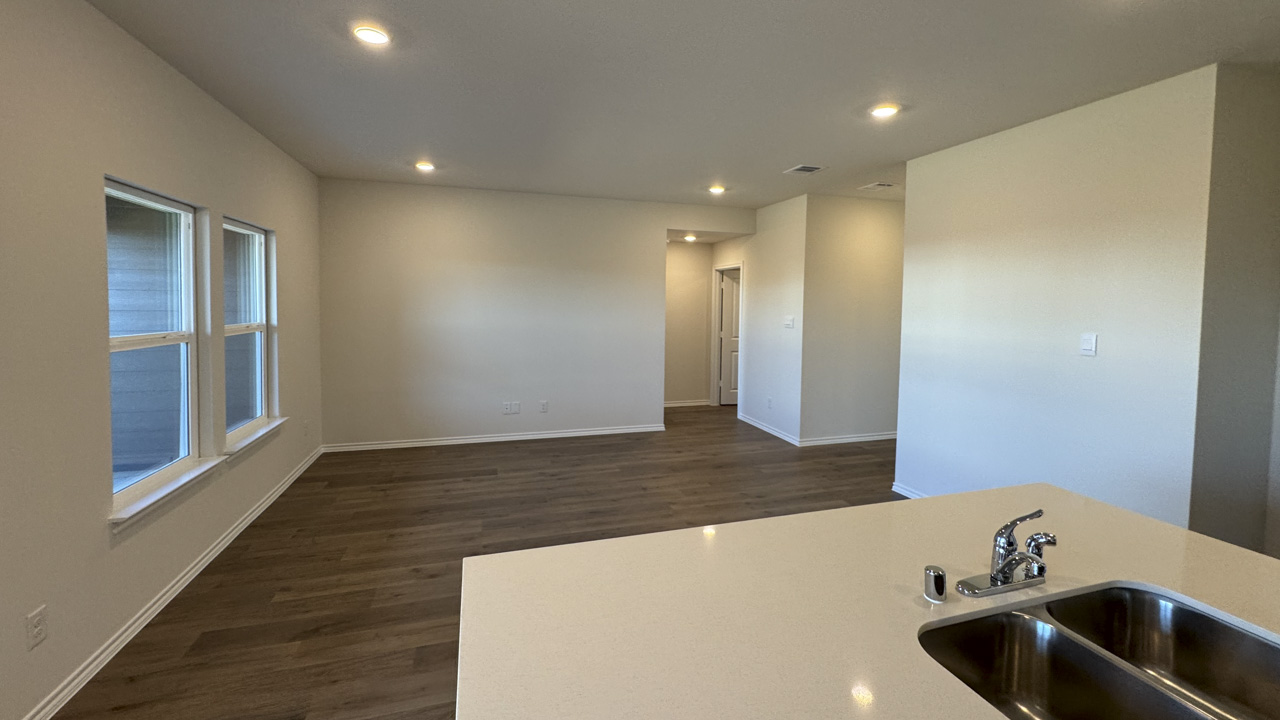 Kitchen island area with white counters facing large living room with hardwood floors