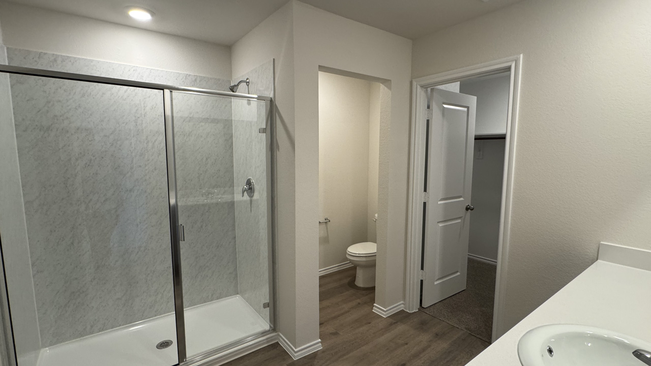 Primary bathroom with hardwood floors glass shower door with white counters and dark cabinets
