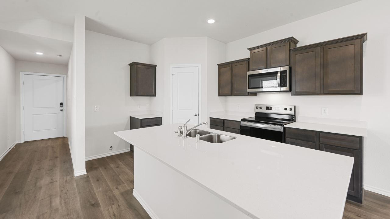 Kitchen area with dark colored cabinets and light colored counters with hardwood floors
