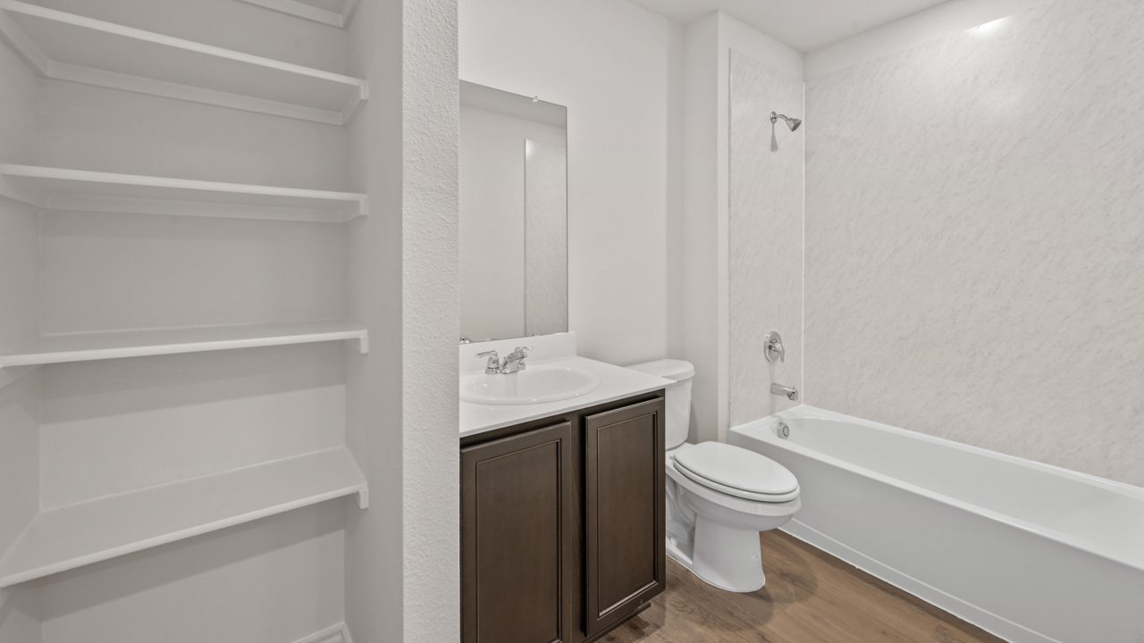 Secondary bathroom with hardwood floors with white counters dark cabinets and white tub with white shelves