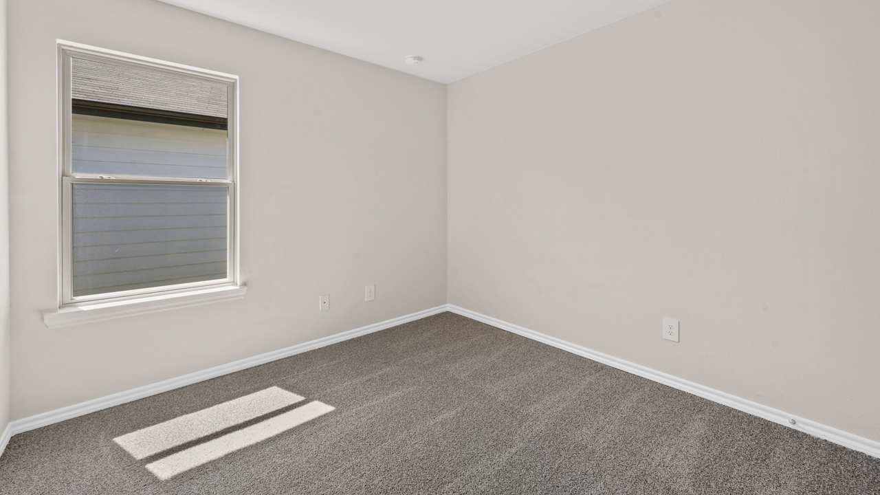 Secondary bedroom with white walls carpet and large window providing natural light