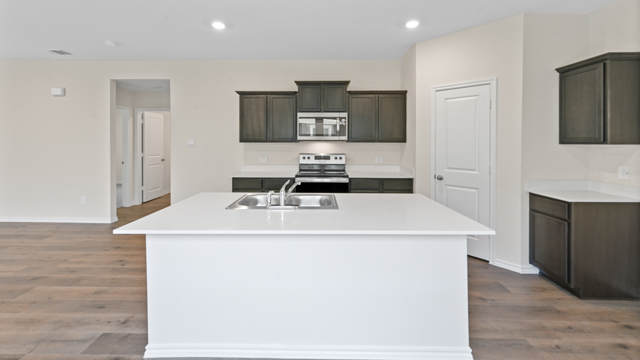 Kitchen area with light colored counters dark cabinets and hardwood floors with kitchen island
