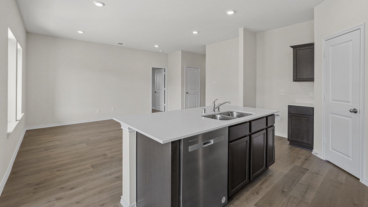 a kitchen with an island in the middle and dark cabinets, white walls and wood floors