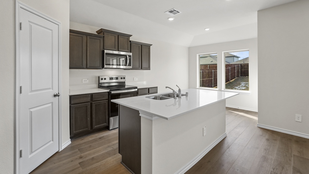 a kitchen with an island in the middle and dark cabinets, white walls and wood floors