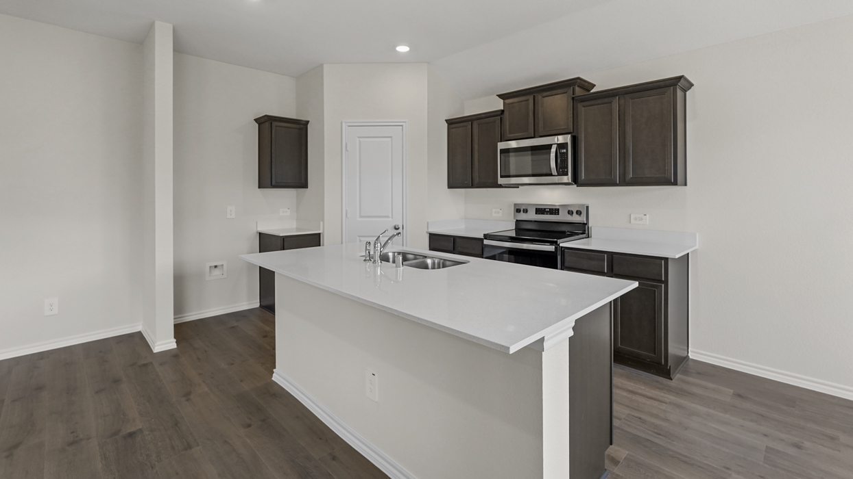 a kitchen with an island in the middle and dark cabinets, white walls and wood floors
