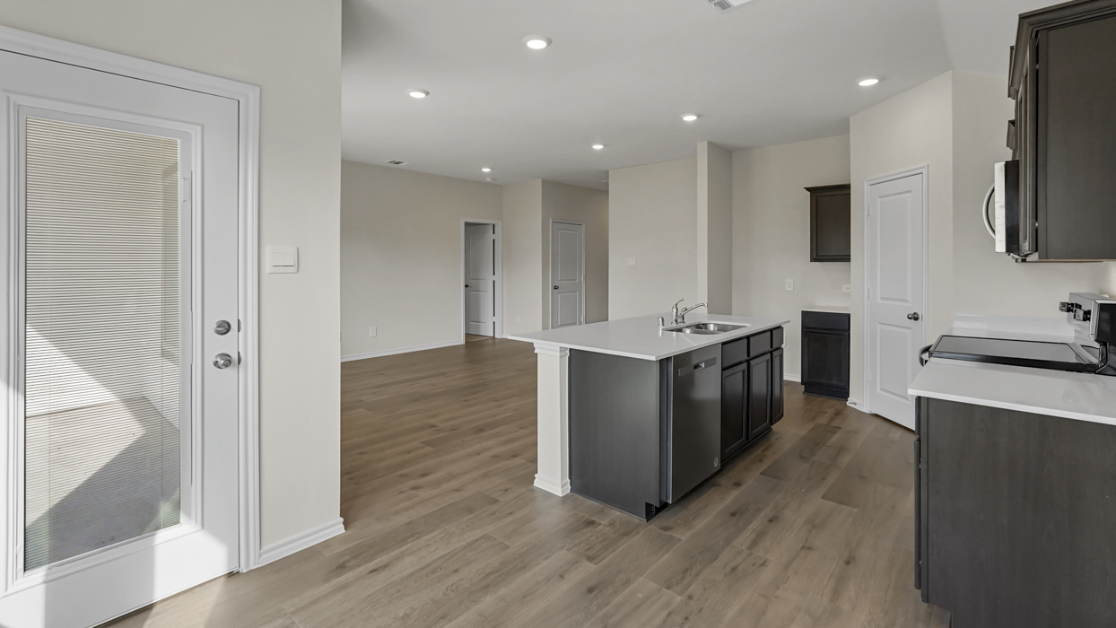 a kitchen with an island in the middle and dark cabinets, white walls and wood floors