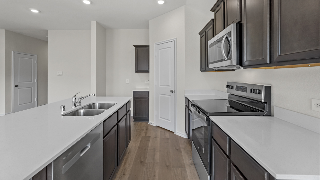a kitchen with an island in the middle and dark cabinets, white walls and wood floors