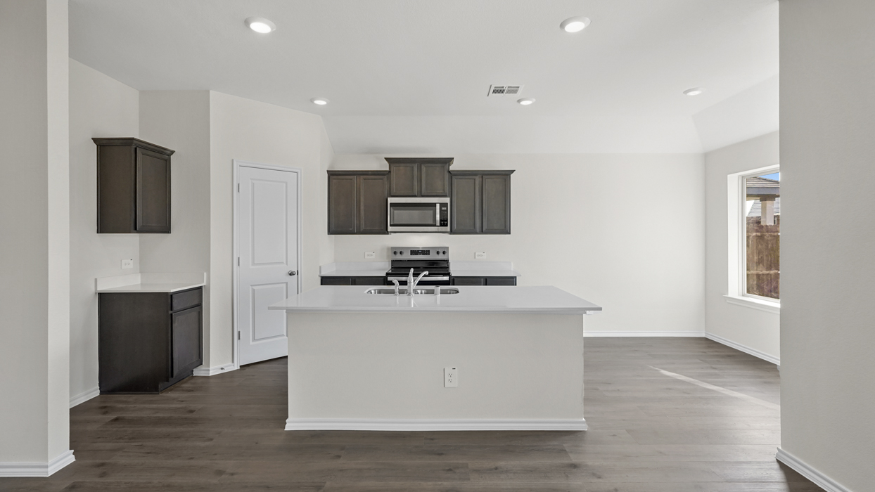 a kitchen with an island in the middle and dark cabinets, white walls and wood floors
