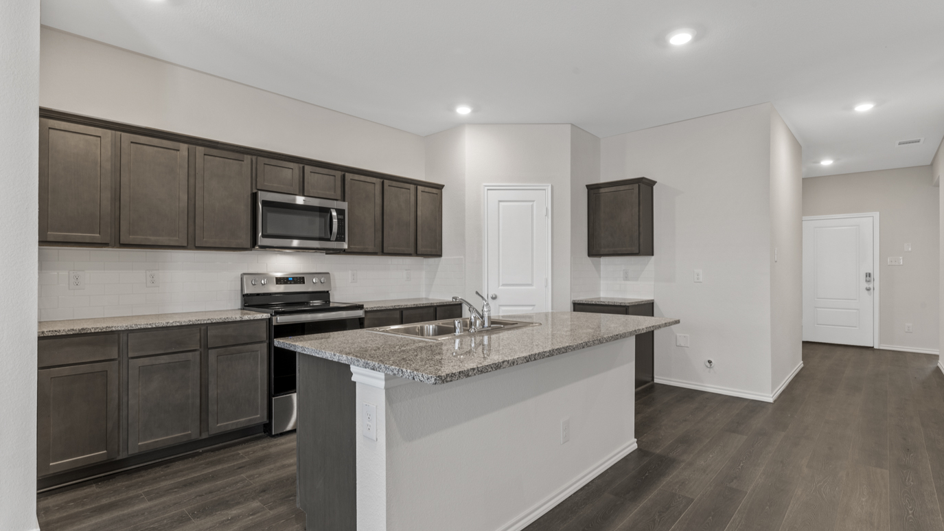 a kitchen with dark cabinets an island in the middle white walls and wood floors