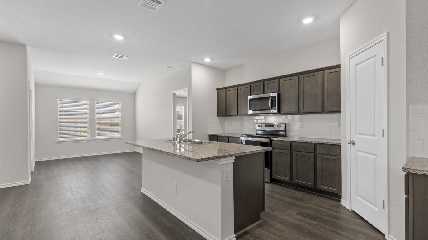 a kitchen with dark cabinets an island in the middle white walls and wood floors