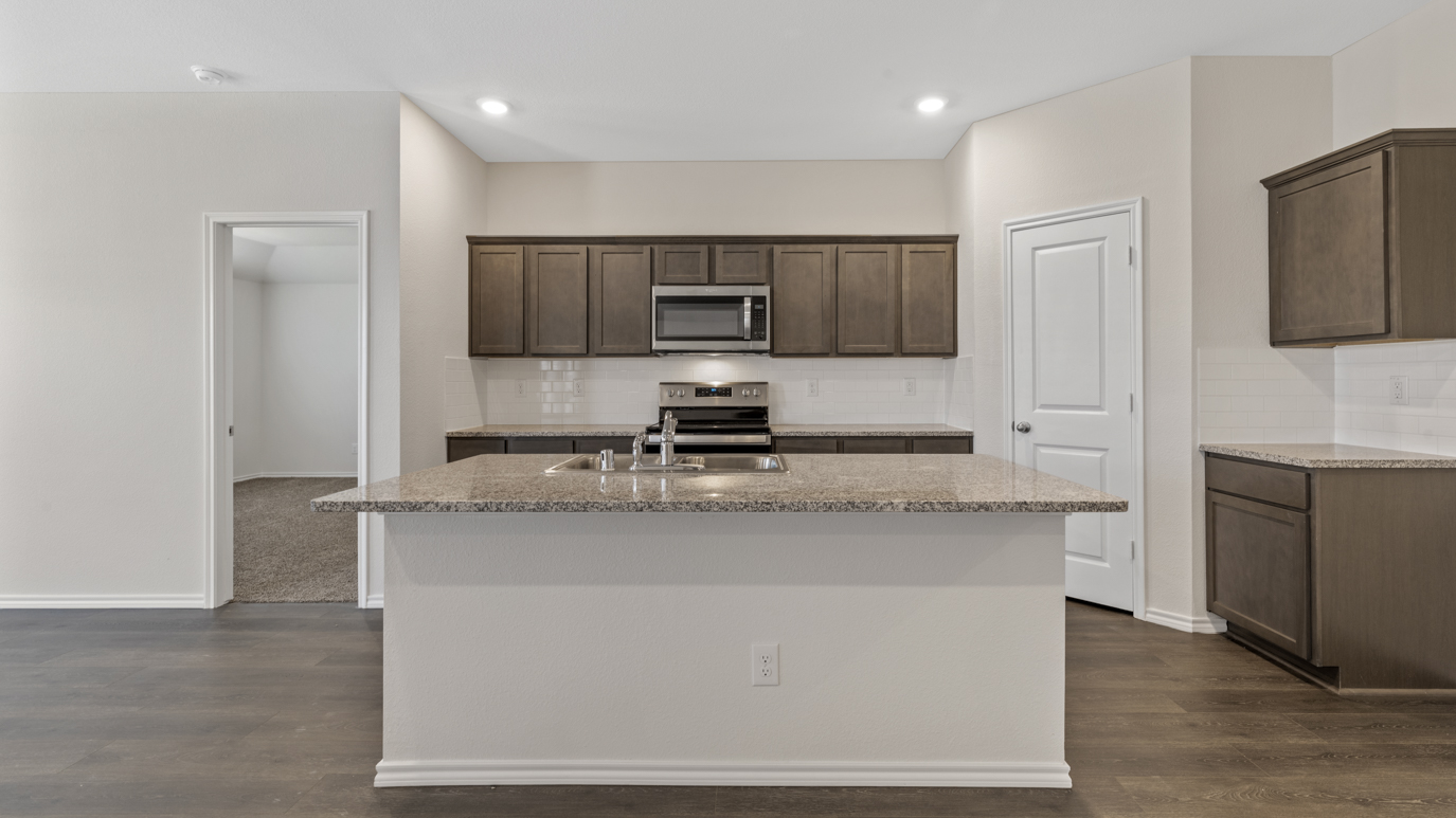 a kitchen with dark cabinets an island in the middle white walls and wood floors