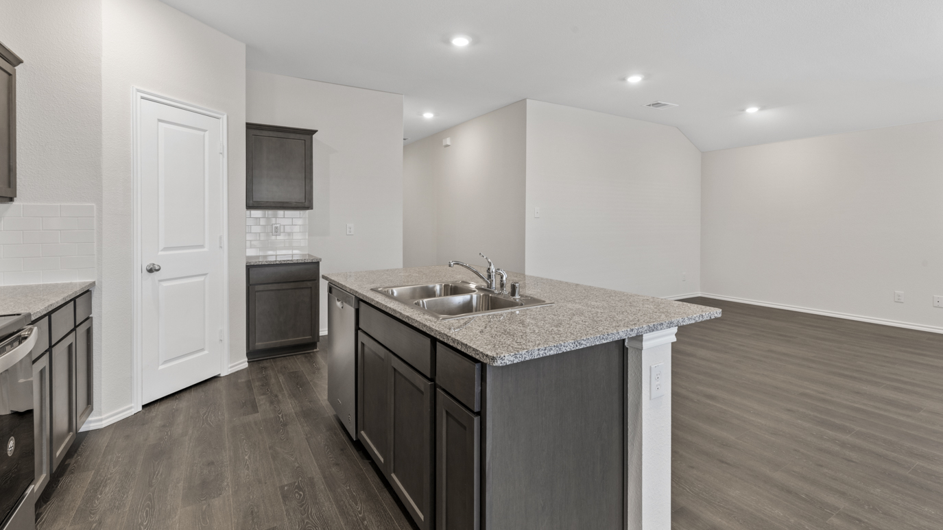 a kitchen with dark cabinets an island in the middle white walls and wood floors