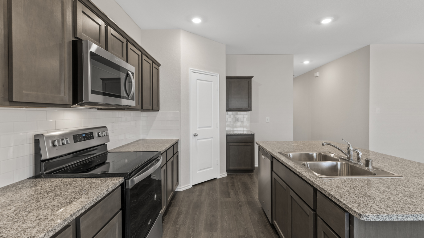 a kitchen with dark cabinets an island in the middle white walls and wood floors