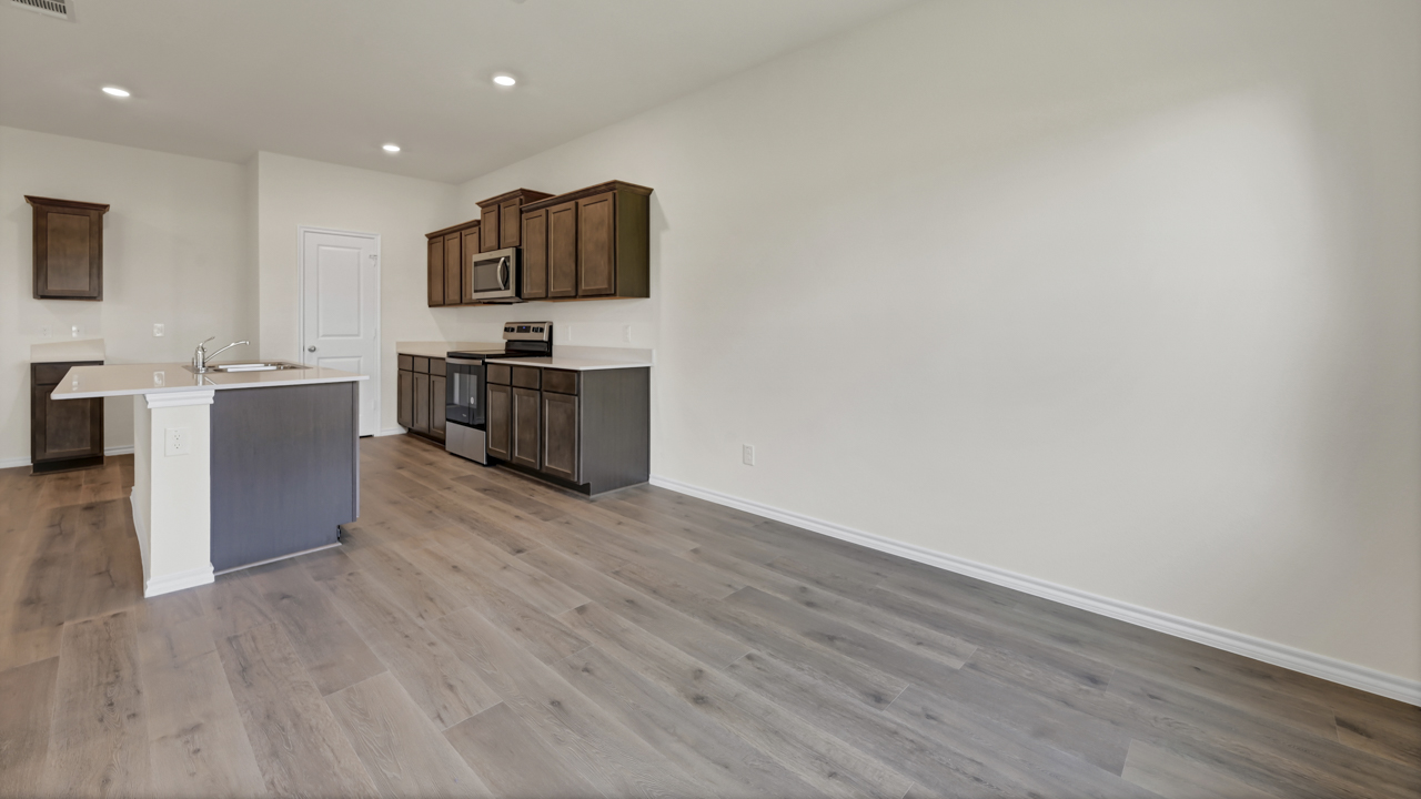 the kitchen of a home with dark cabinets wood floors and white walls with white counter tops and an island in the middle