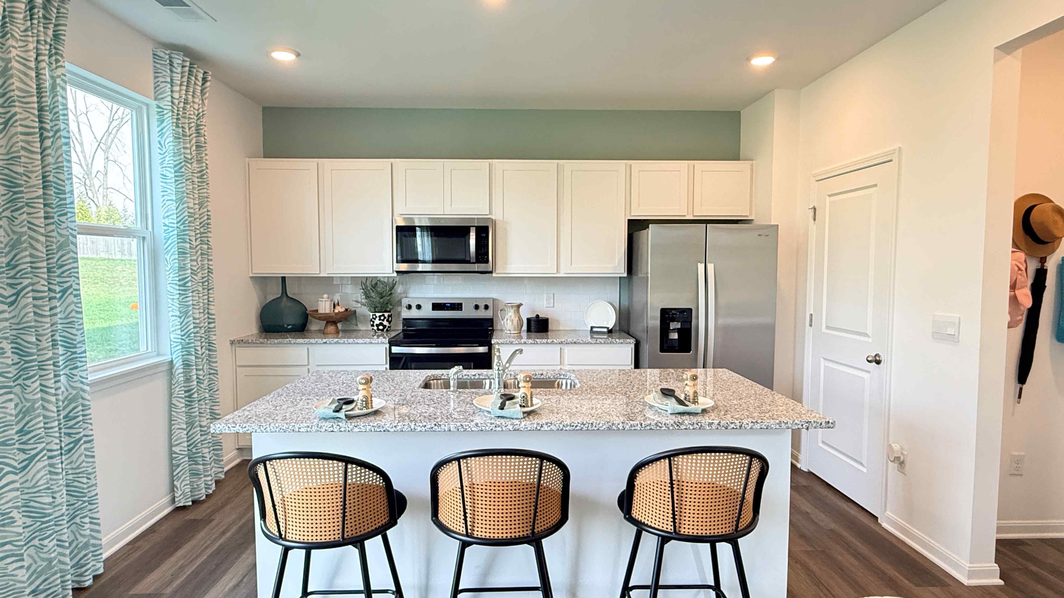 Spacious kitchen with white cabinets, stainless steel appliances, and center island with 3 barstools.