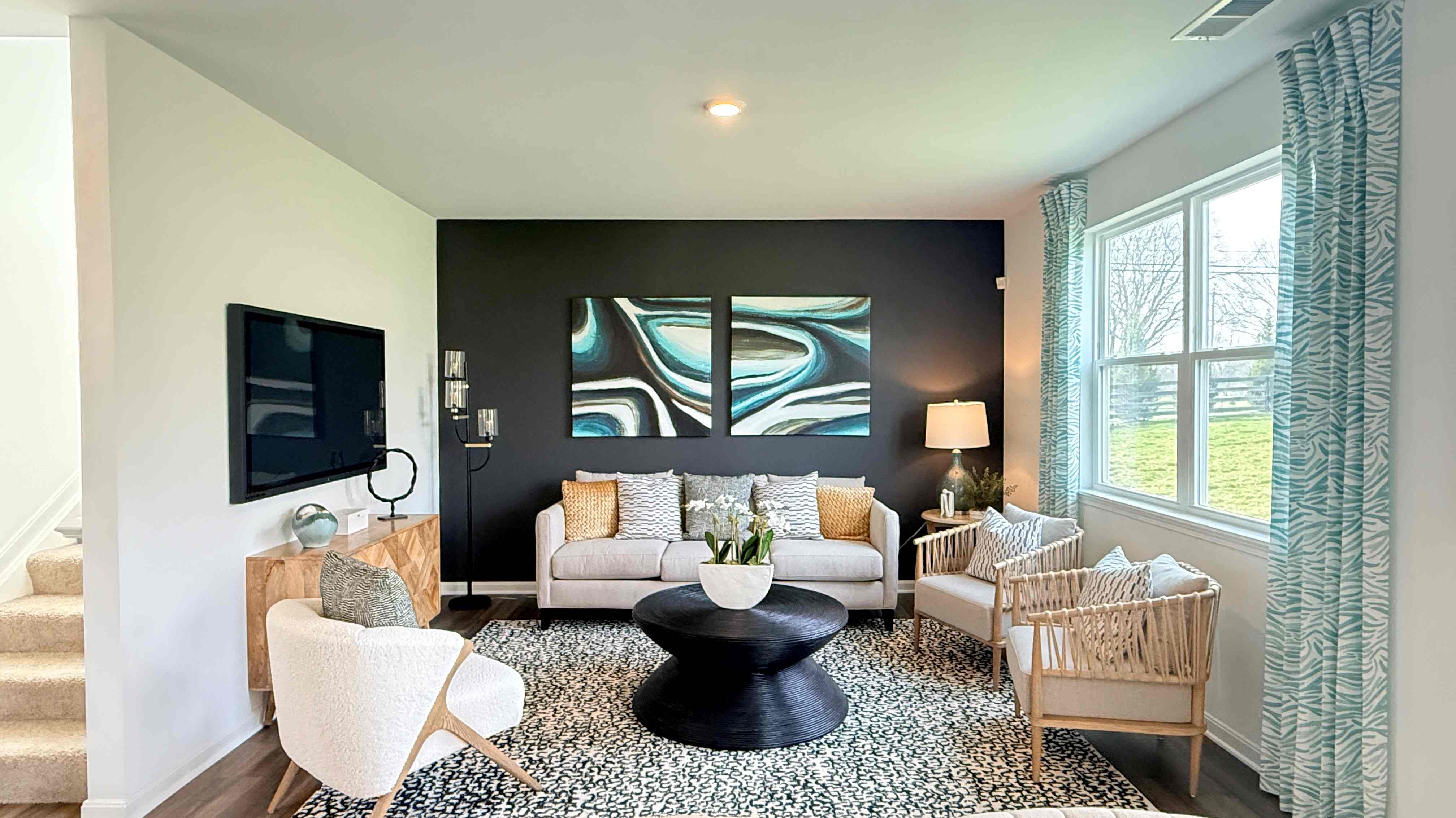 Living room with tv on the wall, couch, 3 accent chairs, coffee table, and double window overlooking the backyard.