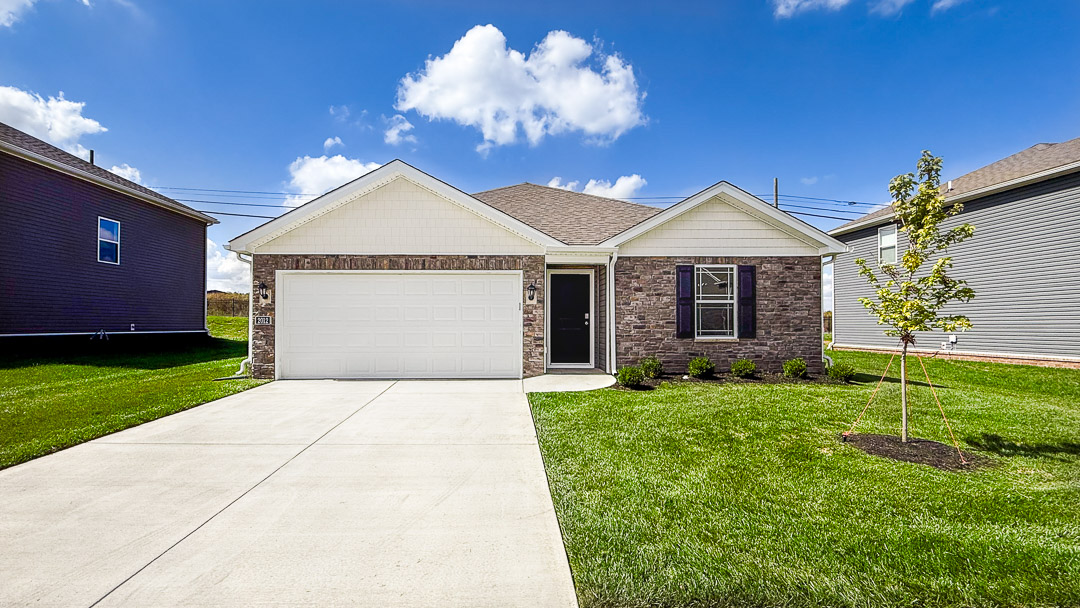 exterior of an all stone ranch home with black shuttered windows, long driveway and tree in the front yard