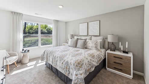 Bedroom with beige carpet, window, bed, and bedside table