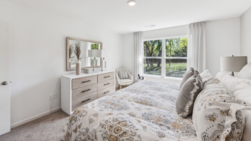 Bedroom with white walls, beige carpet, bed and dresser