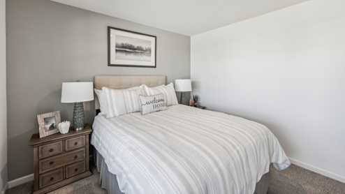 Bedroom with beige carpet, white walls, and brown bedside table