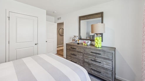 Bedroom with bed, grey dresser and closed closet with white door