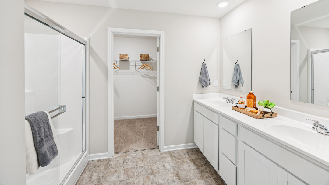 Primary bathroom with white double bowl vanity, closet door, and walk-in shower