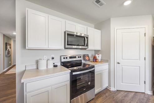 Kitchen with white cabinetry, stainless range and overhead microwave. Closed white pantry door.