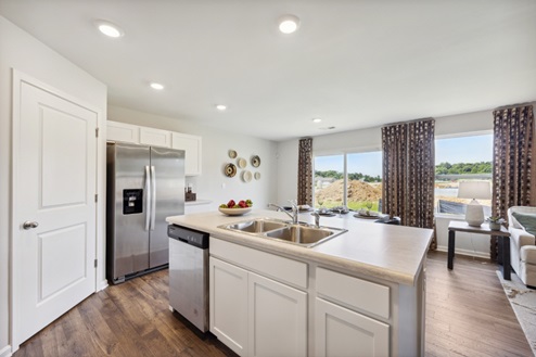 View of open concept living space from white island with sink, stainless refrigerator