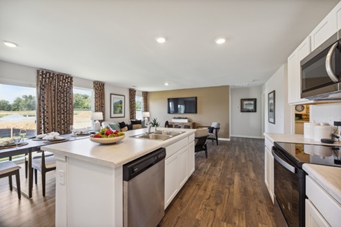 View of of open concept living space from kitchen with white island and stainless dishwasher. Brown vinyl plank flooring.